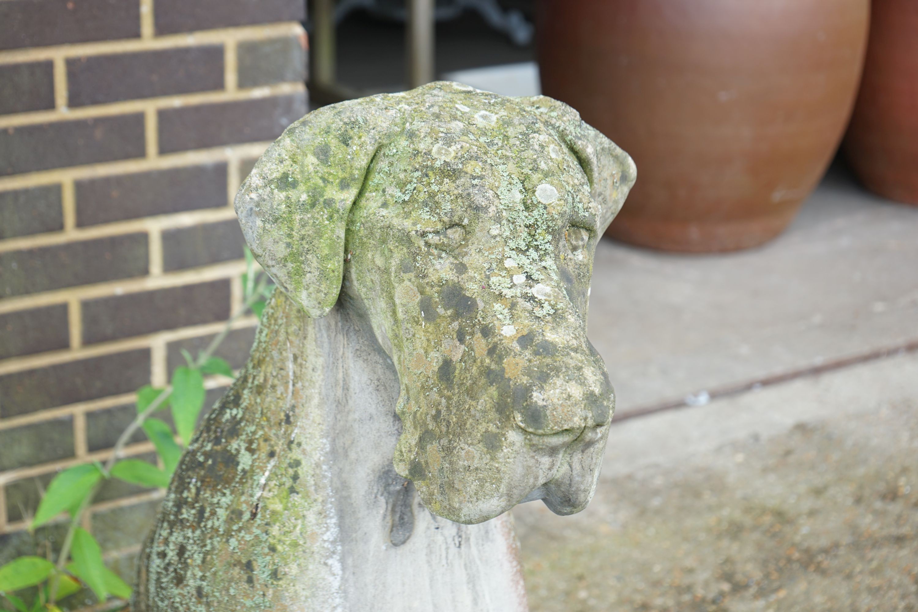 A large weathered reconstituted stone garden ornament modeled as a seated Great Dane, height 116cm